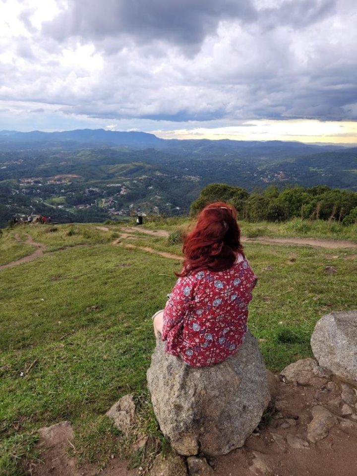 Mulher sentada em pedra olhando a vista.